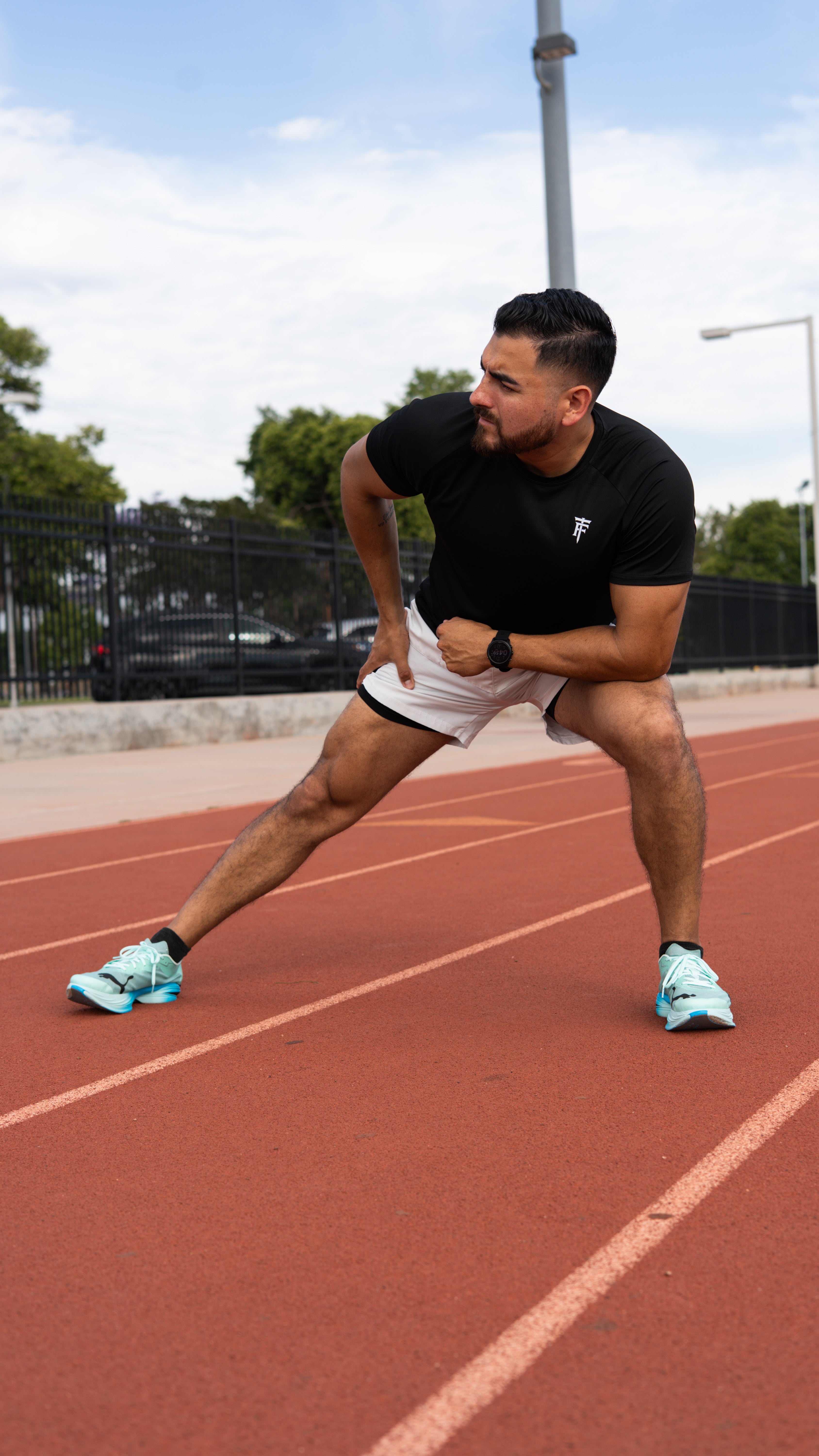 Man stretching on a running track with trees and buildings in the background